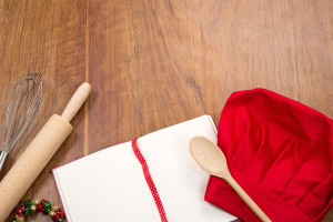 open cookbook, chef's hat and kitchen tools on wood table